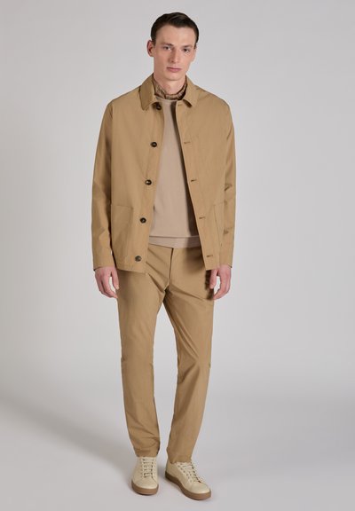 Chaqueta beige clara con botones marrones, combinada con un suéter beige y pantalones a juego. Textura suave, diseño entallado y estilo minimalista.