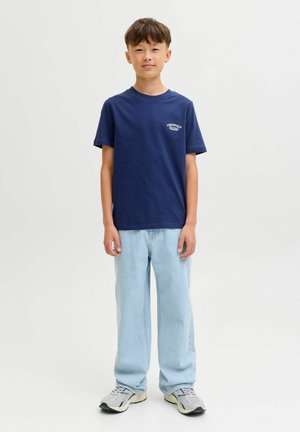 Navy korte mouw t-shirt met logo op de borst, gecombineerd met lichtblauwe wijde jeans en grijze sneakers. Eenvoudige, casual outfit.