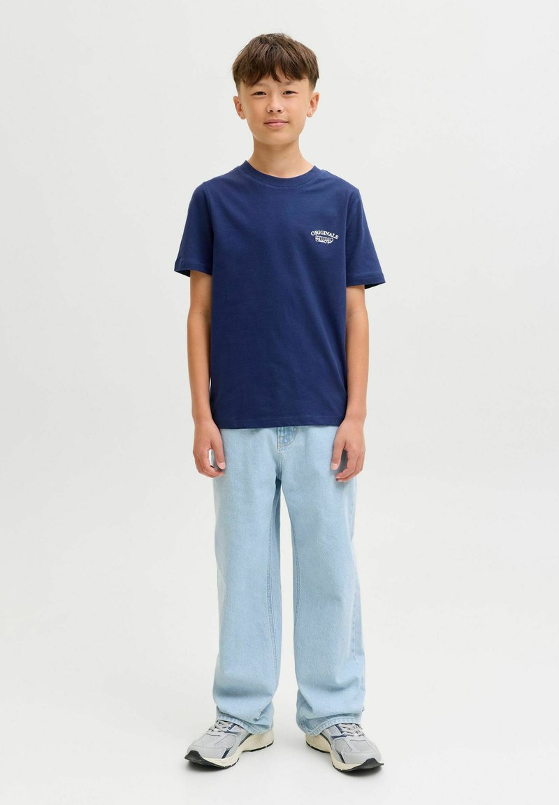 Navy korte mouw t-shirt met logo op de borst, gecombineerd met lichtblauwe wijde jeans en grijze sneakers. Eenvoudige, casual outfit.