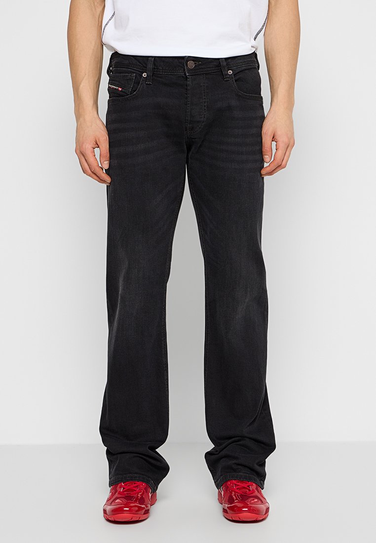 Schwarze Denim-Jeans mit gerader Beinform, Fünf-Taschen-Stil und leichtem Verblassen. Kombiniert mit knallroten Sneakers.