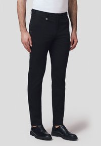 Czarne eleganckie spodnie uszyte z gładkiego, tkane materiału, z dopasowanym krojem, szlufkami na pasek, kieszeniami z przodu oraz zamkiem błyskawicznym. Towarzyszą im czarne buty wizytowe.