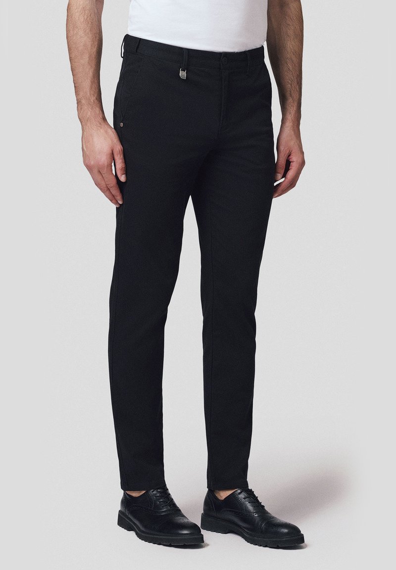 Czarne eleganckie spodnie uszyte z gładkiego, tkane materiału, z dopasowanym krojem, szlufkami na pasek, kieszeniami z przodu oraz zamkiem błyskawicznym. Towarzyszą im czarne buty wizytowe.