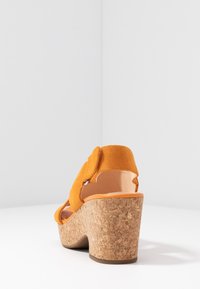 Sandalo wedge in suede arancione con tacco in sughero, apertura sul retro e cinturino alla caviglia, con un dettaglio decorativo in tessuto sulla parte superiore.