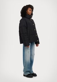 Doudoune noire avec un col haut et des boutons pression dorés, associée à un jean large déchiré bleu clair et des chaussures à plateforme noires.