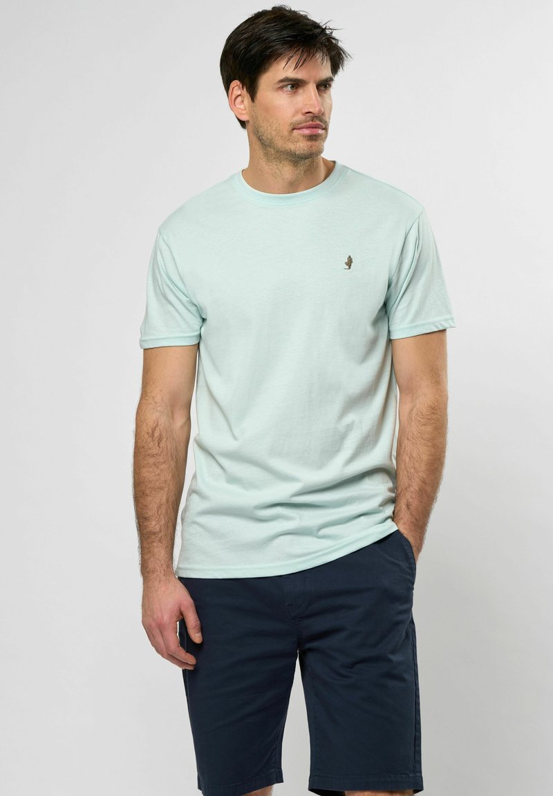 Jasnoniebieska bawełniana koszulka z krótkim rękawem z małym logo na piersi. Noszona z ciemnogranatowymi szortami.