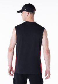 Musta hihaton paita, jossa punaiset sivupaneelit, valmistettu kevyestä kankaasta. Sileä pinta ja pyöreä pääntie. Takakuvassa.