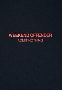 Raudona tekstas "WEEKEND OFFENDER" ir mažesnis "ADMIT NOTHING" atspausdintas tamsiame ridžiuotame audinio fone.