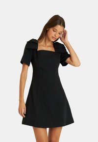 Schwarzes Kleid mit carréförmigem Ausschnitt, kurzen Ärmeln mit Rüschendetails und einem taillierten Oberteil, das zum Saum hin ausgestellt ist. Glatte Stoffstruktur.