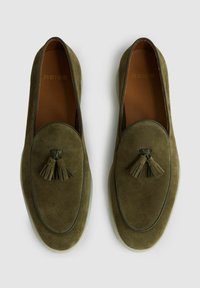 Olijfgroene suede loafers met een ronde neus en een kwastje op de vamp. Gestructureerd oppervlak en een lichtgekleurd loopvlak.
