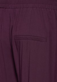 Pantalons bordeaux avec une texture lisse et légère et une taille élastique. Dotés d'une seule poche arrière. Sans motifs ni accessoires visibles.