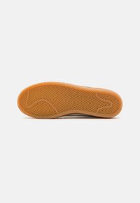 Sola de sapato com uma superfície de borracha texturizada em laranja, apresentando um padrão de espinha de peixe para aderência e suporte. Design plano e largo.