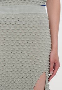 Grijze gebreide jurk met een gestructureerd bobbelpatroon, geribde taille en een golvende zoom met een opening aan de zijkant.