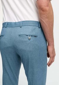 Light blue trousers made of textured fabric, featuring two back pockets with button closures and belt loops. Tailored fit.
