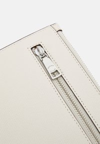 Vit texturerad läderpåse med en framträdande silverfärgad dragkedja med en rektangulär dragtab och detaljerad sömnad längs kanten.