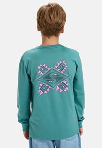 Langärmliges, türkisfarbenes T-Shirt mit einem großen, mehrfarbigen Grafikdesign auf der Rückseite, das geometrische Formen und Akzente in Pink zeigt.