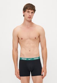 Fekete boxer alsónadrág zöld Nike logós derékkal, sima textúrával és testhezálló kialakítással, amely támogatást nyújt.