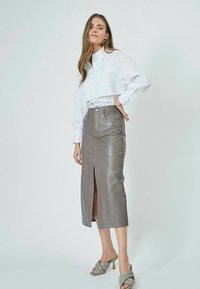 Gonna midi in pelle grigia con uno spacco frontale, abbinata a una camicia bianca con colletto. Sandali con tacco a blocco completano il look.