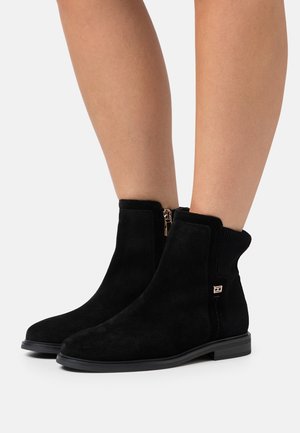 Bottines en suède noir avec une texture lisse, des panneaux latéraux élastiques et un détail en zip doré, dotées d'une semelle en caoutchouc plate.