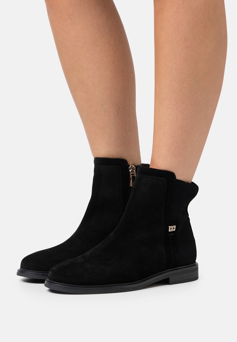 Stivaletti neri in suede con una texture liscia, pannelli laterali elastici e un dettaglio di zip dorata, dotati di suola piatta in gomma.