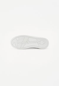 Semelle de sneaker blanche présentant une surface en caoutchouc texturée avec un motif en zigzag et un logo en relief au centre. Design plat et arrondi.