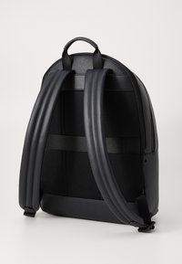 Black backpack with a textured finish, padded adjustable straps, mesh back panel, and zipper closure. Smooth accents enhance durability.