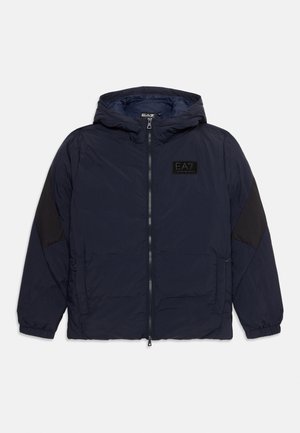 Tengerészkék pufi kabát kapucnival, fekete válldíszítéssel és elülső cipzárral. EA7 logóval ellátott folt és oldalzsebek találhatók rajta.