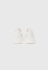 Baskets en cuir blanc avec des semelles blanches épaisses. Présentent une texture lisse et des onglets de tirage au talon. Design minimaliste sans motifs visibles.