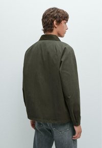 Olijfgroene jas met een kraag, rechte snit en een gladde textuur. Draag over grijze denim, met een casual ontwerp en minimale accenten.