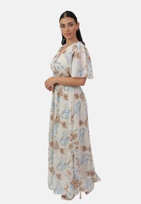 Robe longue à fleurs avec un fond blanc et des motifs de fleurs bleues et brunes, à manches bouffantes courtes et taille ajustée.