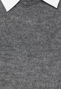 Pull en maille gris avec une texture côtelée et un col blanc, présentant des détails de couture visibles. Design doux et décontracté.