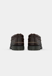 Par de sapatos de barco em pele castanha escura com detalhes cosidos e solas de borracha preta, vistos por trás sobre um fundo branco.