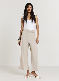 Pantaloni beige a gamba larga con vita drappeggiata e dettaglio annodato. Abbinati a un top aderente bianco senza maniche e sandali con punta aperta.