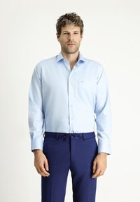 Camicia azzurra a maniche lunghe con bottone e tasca, abbinata a pantaloni eleganti blu scuro con vita regolabile.