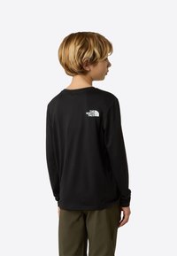 Cămașă neagră cu mâneci lungi, realizată dintr-un material moale. Are un logo alb pe partea superioară a spatelui, guler rotund și manșete strâmte.