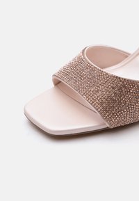 Sandale beige à bout ouvert avec une large bride scintillante couleur or rose couverte de petits strass brillants, talon bloc minimaliste et design à bout carré.