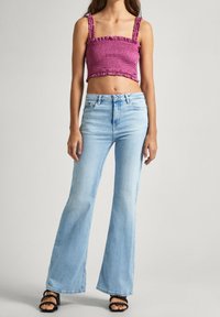 Figurerad, smockad, lavendelfärgad crop top med volangärmar, i kombination med ljusblå utsvängda jeans och svarta klacksandaler med remmar.