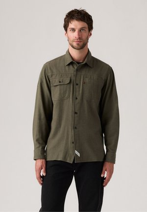 Olive green long-sleeve shirt with two chest pockets, button front, and textured fabric. Paired with black pants.