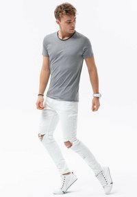 Grå t-shirt med sort halsudskæring, parret med hvide ripped jeans og hvide sneakers. Casual pasform med let tekstur på stoffet.