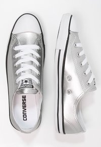 Metallisch silberne Leinenschuhe mit weißen Schnürsenkeln, schwarzen Akzenten und einer Gummispitze. Verfügt über ein klassisches Low-Top-Design und Ösen.