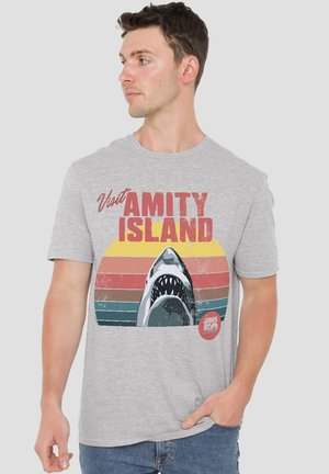 Gray t-shirt featuring a graphic of a shark and retro stripes in orange, yellow, and teal. Text reads "Visit Amity Island."