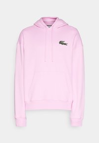 Sweat à capuche rose clair avec poche avant et capuche à cordon, présentant un petit logo crocodile vert sur la poitrine.