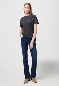 T-shirt en coton noir à manches courtes avec un logo imprimé sur la poitrine, associé à un jean slim bleu foncé et des bottines beige.