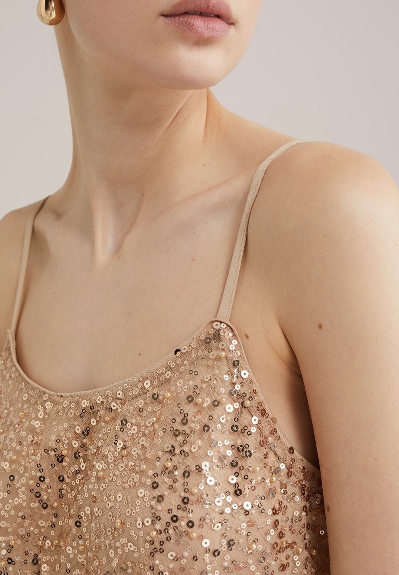 Naga bluzka z cekinami na cienkich ramiączkach, ozdobiona rozrzuconymi metalicznymi cekinami w odcieniach złota i brązu na przezroczystym materiale.
