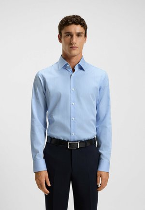 Hellblau gestreifte Langarmbluse mit Kragen, Knopfverschluss und weichem Stoff. Getragen mit dunklen Hosen und einem schwarzen Gürtel.