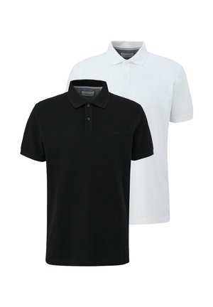 Hombre con polo blanco de manga corta, pantalones cargo negros y zapatillas blancas, de pie con una mano en el bolsillo.