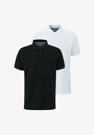 Uomo che indossa una polo bianca a manica corta, pantaloni cargo neri e sneakers bianche, in piedi con una mano in tasca.