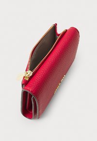 Portofel roșu din piele cu suprafață texturată, fermoar și accesorii aurii, deschis pentru a revela un interior maro. Design compact cu o închidere sigură.