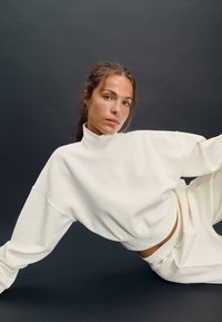 Felpa bianca con collo alto, dal fit ampio, con una texture morbida e spalle cadute, abbinata a pantaloni con elastico in vita coordinati.