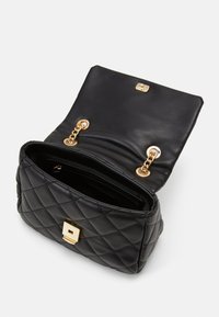 Sac à main en cuir matelassé noir avec un fermoir carré en or et des accents en chaîne. Le haut ouvert révèle un intérieur spacieux avec plusieurs compartiments.