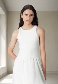 White sleeveless dress with a fitted bodice and flared skirt, featuring a smooth texture and subtle seam detailing.